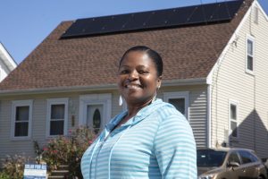 Sophia smiling outside their home, which has a rooftop solar array