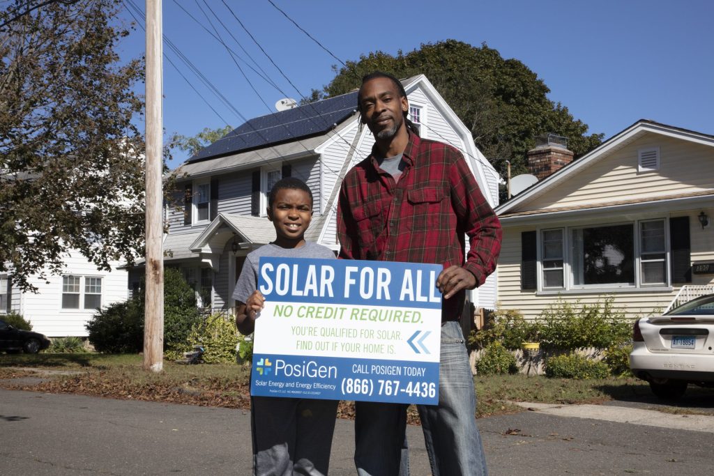 Chad and Justin standing beside a Solar for All yard sign outside their home